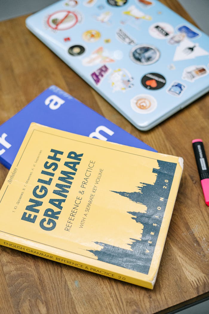 classes-02 High-angle view of an English grammar book and a laptop with stickers on a wooden desk.