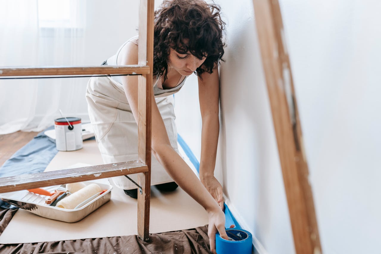 class-03 Woman uses tape to prep wall for painting, part of a DIY home renovation project indoors.